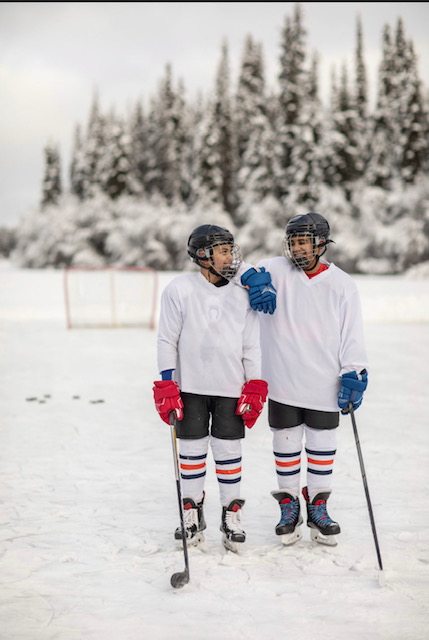 two men in hockey gear on a frozen lake with trees behind them